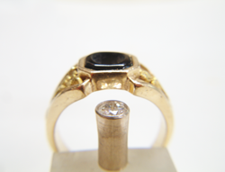 Side view of a nugget style ring with a black Onyx in the middle and a Diamond in a gold tube next to the ring.