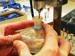 A photo of me using my drill press to drill a stopper out of an antique glass bottle.