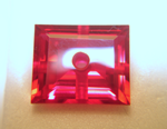 Photo of a red synthetic Ruby with a hole drilled in the center.