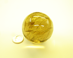 Shows the Rutillated Quartz sphere sitting next to a dime for size comparison.