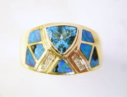 Photo of a ring with a blue Topaz center stone and many triangular Opal inlays, some of which are broken.