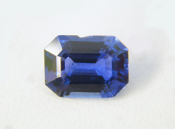 An emerald cut blue Sapphire with a chip along the side.