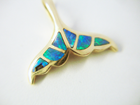 Photo of a pendant in the shape of a whale tail which is missing one of the opal inlays.